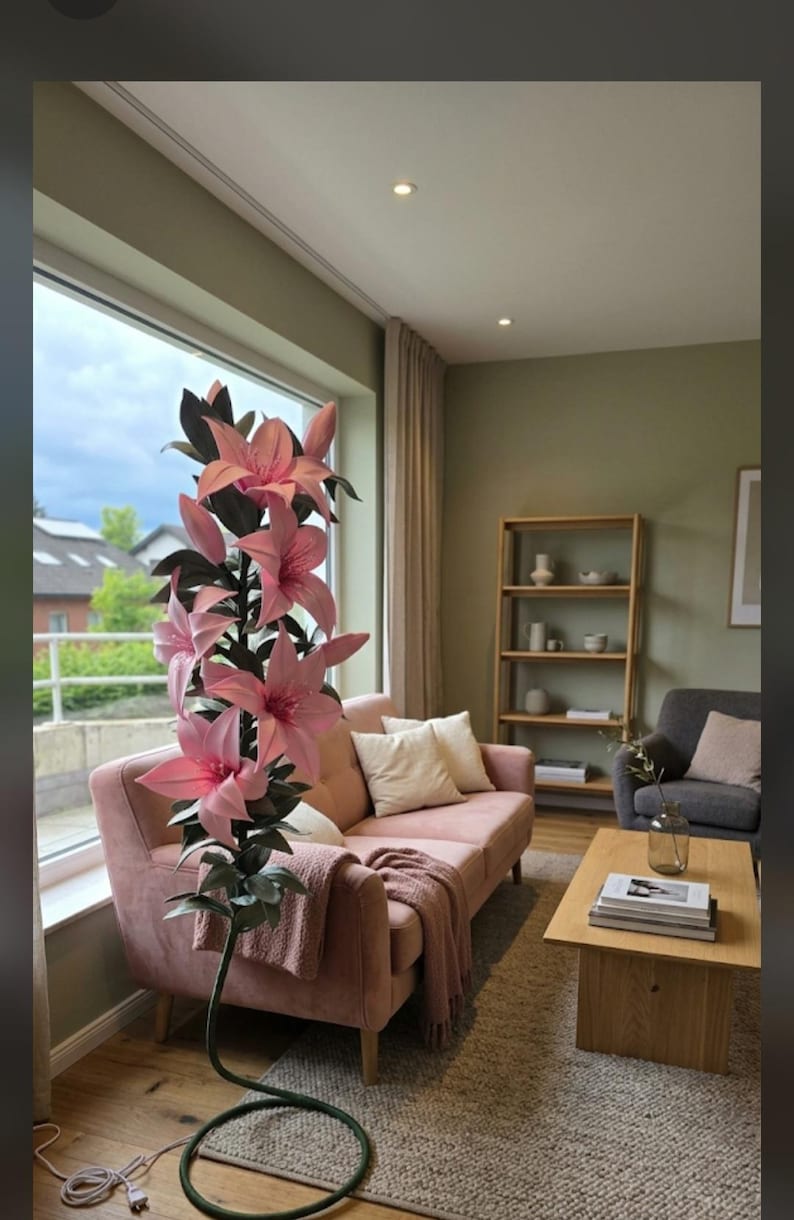 Puede incluir: Una planta artificial alta de pie que presenta m&uacute;ltiples flores de lirio de color rosa vibrante con hojas de color verde oscuro sobre un tallo delgado de color verde oscuro que se curva en una base circular con un cable el&eacute;ctrico blanco.