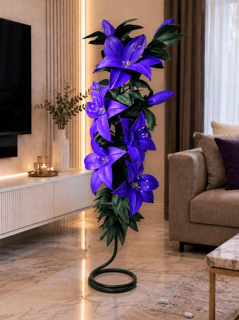 Puede incluir: Una l&aacute;mpara de pie alta con forma de racimo de flores de lirio de color p&uacute;rpura vibrante con hojas de color verde oscuro. La l&aacute;mpara cuenta con una base negra en espiral que descansa en el suelo, con un cable blanco fino desde la base.