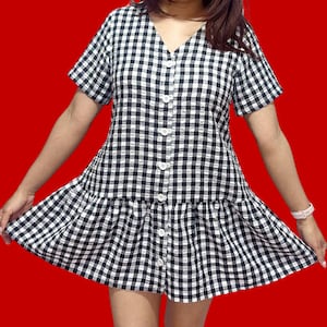 Puede incluir: Un vestido de botones de cuadros negros y blancos con un dobladillo con volantes.