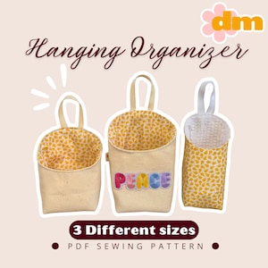 May include: Three beige hanging organizers with fabric lining. The organizers have a handle and are in different sizes. One organizer has the word "PEACE" in colourful letters. The text "Hanging Organizer" is at the top.