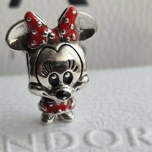 K&ouml;nnte beinhalten: Ein silberner Charm-Anh&auml;nger, der Minnie Mouse darstellt, mit einer roten Schleife mit wei&szlig;en Punkten und einem passenden roten Kleid mit wei&szlig;en Punkten. Der Charm hat ein detailliertes Gesicht und ist ein Sammlerst&uuml;ck.