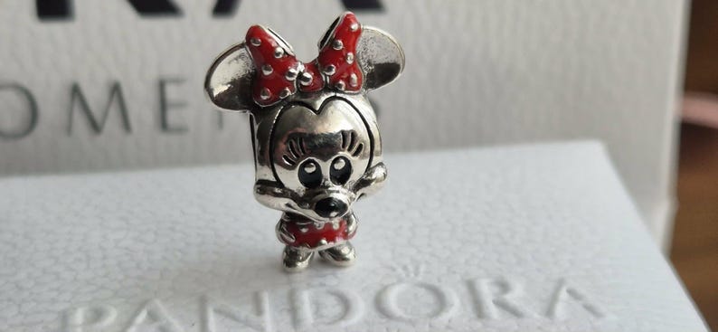 K&ouml;nnte beinhalten: Ein silberner Charm-Anh&auml;nger, der Minnie Mouse darstellt, mit einer roten Schleife mit wei&szlig;en Punkten und einem passenden roten Kleid mit wei&szlig;en Punkten. Der Charm hat ein detailliertes Gesicht und ist ein Sammlerst&uuml;ck.