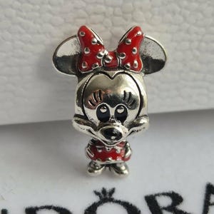 K&ouml;nnte beinhalten: Ein silberner Charm-Anh&auml;nger mit Minnie Mouse, mit roter Schleife und Kleid mit Tupfen. Der Charm hat ein detailliertes Design mit schwarzen Augen und einem l&auml;chelnden Ausdruck. Ein Sammlerst&uuml;ck.