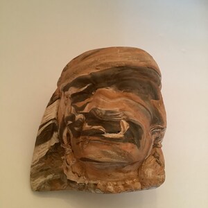 May include: A brown and white ceramic sculpture of a face with a textured surface.