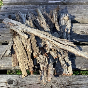 May include: A pile of bark pieces, some with rough edges, on a weathered wooden surface. The bark is a light brown color and has a natural, rustic look.