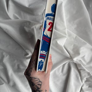 May include: A book spine featuring a blue and red illustration of a football player with the number 2. The word "HOLL" is printed above the number. The book has a white spine and a cream-colored cover.