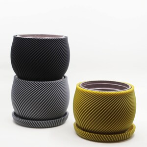 May include: Three plant pots with a spiral design. The top pot is black, the middle pot is gray, and the bottom pot is yellow.