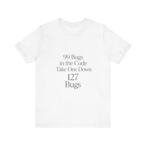 Könnte beinhalten: Ein weißes Kurzarm-T-Shirt mit dunkelgrauem Text, der mittig auf der Brust gedruckt ist: 99 Bugs in the Code Take One Down 127 Bugs. Das Kleidungsstück hat einen Rundhalsausschnitt und eine Standardpassform, was ein schlichtes Design ergibt.