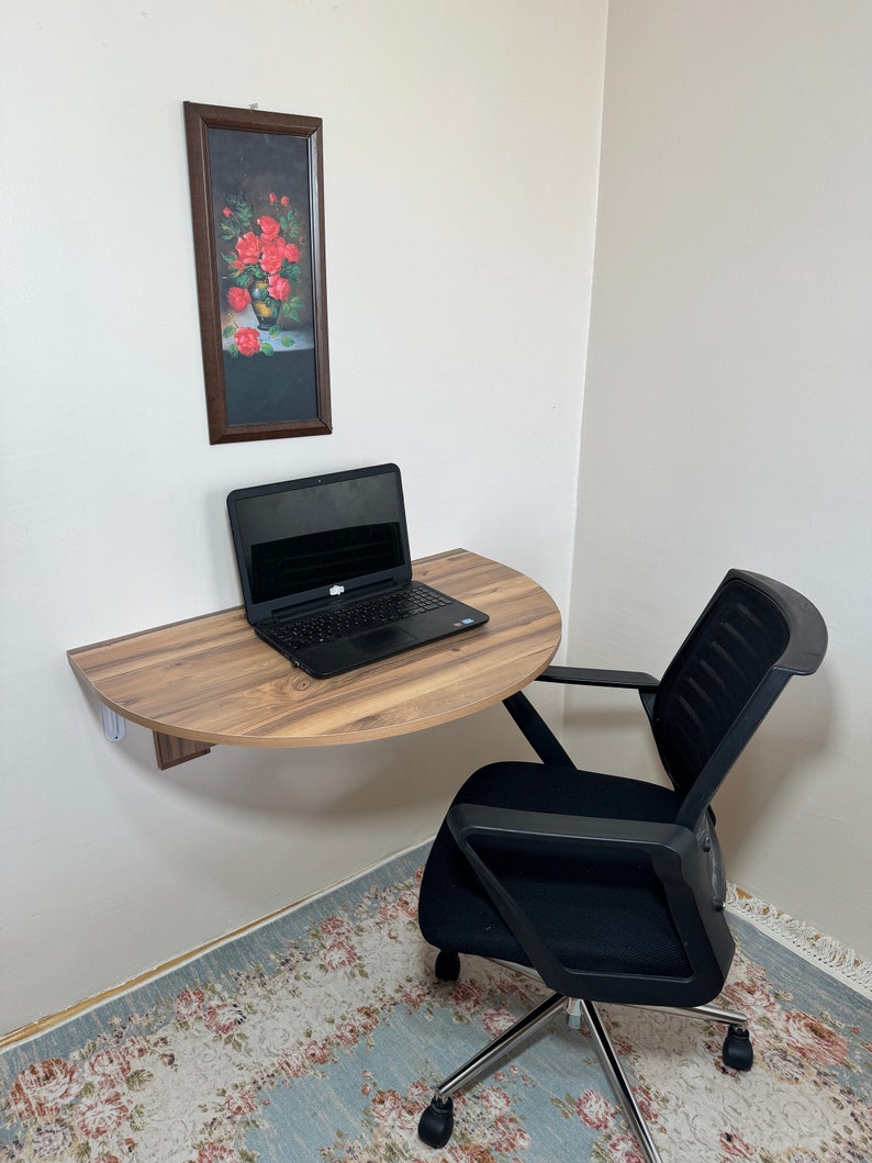 Pu&ograve; includere: Una piccola scrivania semicircolare in legno, montata a parete, con un laptop sopra. Una sedia da ufficio nera &egrave; posizionata sotto la scrivania. Un dipinto incorniciato di rose rosse &egrave; appeso al muro. La stanza ha un tappeto con motivi floreali.
