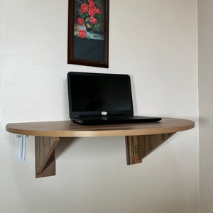Pu&ograve; includere: Una scrivania in legno semicircolare montata a parete con un laptop sopra. La scrivania &egrave; sostenuta da due staffe triangolari. Sopra la scrivania c'&egrave; un dipinto incorniciato di rose rosse in un vaso. Il muro &egrave; di colore beige chiaro.