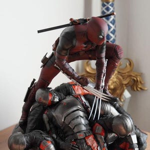 以下が含まれることがあります： ダイナミックなポーズのデッドプールの詳細なフィギュア。赤と黒のスーツを着て、爪を持っています。フィギュアは、黒と赤の鎧を着た複数のフィギュアの上にあります。デッドプールの背中には剣が取り付けられています。