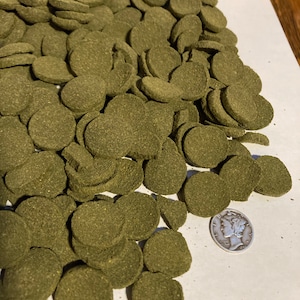 May include: A large pile of green, round fish food pellets. A silver US dime is included for scale.