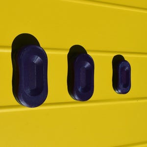 May include: Three dark blue, oval-shaped objects are set into a bright yellow surface. The objects are of varying sizes, with the largest on the left and the smallest on the right. The yellow surface has horizontal lines.