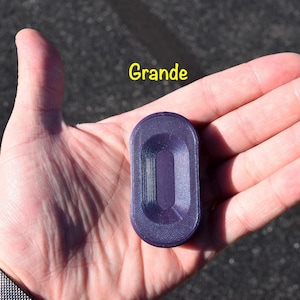 May include: A purple, rectangular object with rounded edges is held in a person's hand. The object has a recessed centre and the word "Grande" is written in yellow above it. The object appears to be made of plastic.