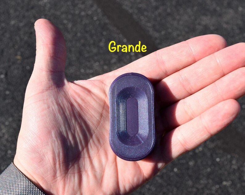 May include: A purple, rectangular object with rounded edges is held in a person's hand. The object has a recessed centre and the word "Grande" is written in yellow above it. The object appears to be made of plastic.