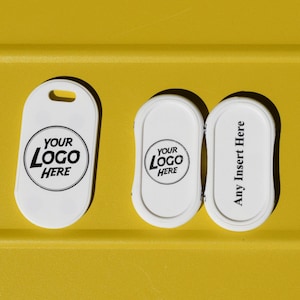 May include: Three white plastic oval-shaped tags with black printed text. One tag features a hole at the top and the text "YOUR LOGO HERE". The other two tags feature the text "YOUR LOGO HERE" and "Any Insert Here" respectively.