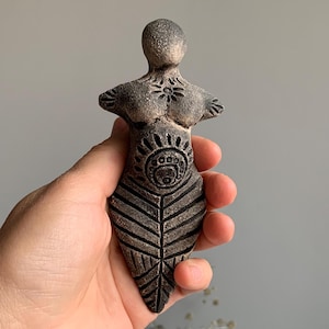 May include: A small, hand-crafted ceramic figurine of a woman with a stylised leaf design and intricate details. The figurine is painted in shades of brown and black.
