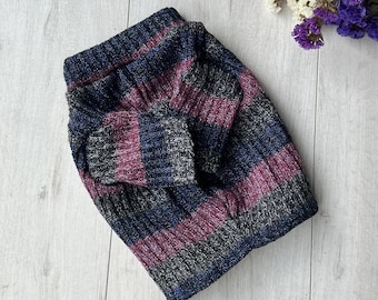 May include: A folded knit hat with horizontal stripes in navy blue, gray, and burgundy. The hat is made of a ribbed knit fabric and has a folded brim. The hat is lying on a light wood surface.