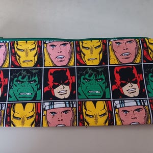 May include: A green zippered pencil case with a repeating pattern of comic book characters, including Thor, Iron Man, Hulk, and Daredevil. The characters are in red, yellow, green, and black.