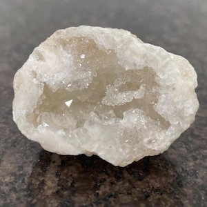 May include: A geode with a crystalline interior and a rough, white exterior. The interior features a light tan colour with visible crystal formations. The geode is an irregular, rounded shape, showcasing natural mineral beauty.