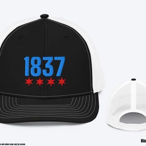 May include: A black and white trucker hat with a blue and red embroidered design. The design features the number "1837" and three red stars.