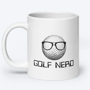 May include: White ceramic coffee mug with a black and white illustration of a golf ball wearing glasses. The text "GOLF NERD" is printed below the golf ball.