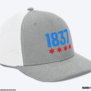 May include: A heather grey and white trucker hat with a blue and red embroidered design. The design features the number "1837" and five red stars.