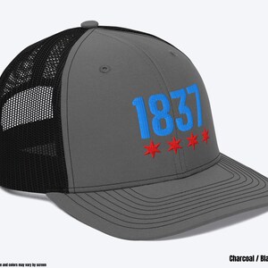 May include: A charcoal gray and black trucker hat with a blue embroidered "1837" and five red stars.