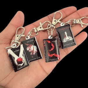 May include: A collection of miniature book keychains showcasing the covers of the Twilight Saga books: Twilight, New Moon, Eclipse, and Breaking Dawn. Each keychain has a silver clasp. The book covers feature images and titles by Stephenie Meyer.