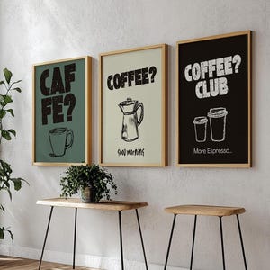 Puede incluir: Tres impresiones enmarcadas con ilustraciones de temática de café. Las impresiones están colgadas en una pared blanca sobre una mesa de madera con patas de metal negro. Las impresiones presentan el texto "Cafe?", "Coffee? Good Morning", y "Coffee? Club More Espresso..."