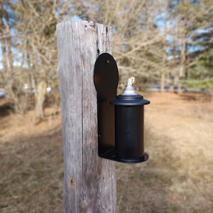 May include: A black metal torch holder mounted on a wooden post. The torch is made of metal and has a silver top.