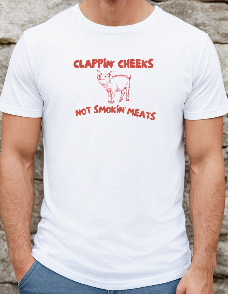 May include: White t-shirt with a red graphic of a pig and the text "CLAPPIN' CHEEKS NOT SMOKIN' MEATS".