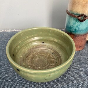 May include: A set of three ceramic mugs with a speckled, cream-colored glaze. Each mug features a different hand-painted floral design in shades of blue, green, and yellow. The mugs have a simple, rounded shape and a comfortable handle.