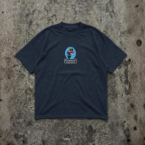 K&ouml;nnte beinhalten: Marineblaues T-Shirt mit einem kreisf&ouml;rmigen Logo, das einen Tukan, zwei blaue Gl&auml;ser und den Text "Guinness" zeigt. Das Logo ist mittig auf der Brust platziert. Das Shirt hat kurze &Auml;rmel und einen Rundhalsausschnitt.