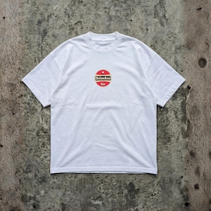 Pu&ograve; includere: T-shirt bianco con girocollo e maniche corte. La maglietta presenta un logo circolare al centro con colori rosso, bianco e oro. Il logo include il testo "Heineken" e "bier".