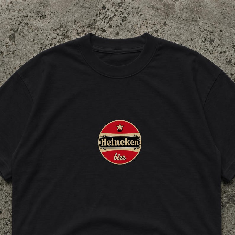 Peut inclure: T-shirt noir avec un logo circulaire "Heineken bier". Le logo est rouge avec un bord dor&eacute; et une &eacute;toile. Le t-shirt est en mati&egrave;re souple. Le texte "bier" est en &eacute;criture cursive.