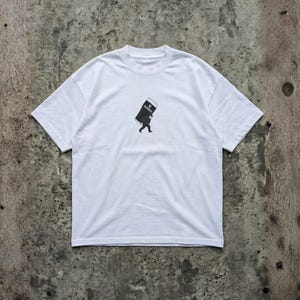 Puede incluir: Camiseta blanca con un gr&aacute;fico en blanco y negro de una persona que lleva una pinta grande de Guinness. El logotipo de Guinness es visible en la pinta. La camiseta tiene mangas cortas y cuello redondo.