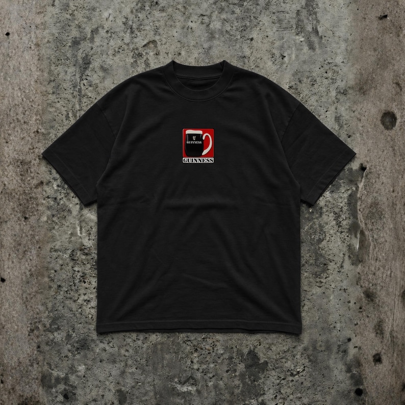 May include: Black t-shirt featuring the Guinness logo. The logo is a red square with a white and black design of a pint of Guinness, with the word "Guinness" below it in white text.