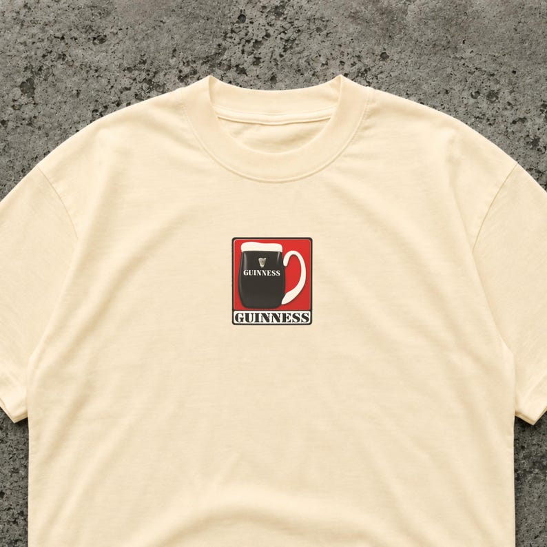 K&ouml;nnte beinhalten: Cremefarbenes T-Shirt mit einem Aufdruck eines Guinness-Pints in einem roten Quadrat. Das Pint ist schwarz mit einem wei&szlig;en Kopf, darunter steht das Wort "Guinness" in Wei&szlig;.