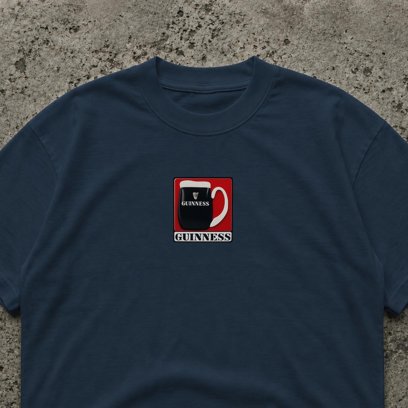 Puede incluir: Camiseta azul marino con un gr&aacute;fico de pinta de Guinness en un cuadrado rojo. La pinta es negra con espuma blanca, y la palabra "Guinness" est&aacute; impresa debajo en blanco. Estilo casual.