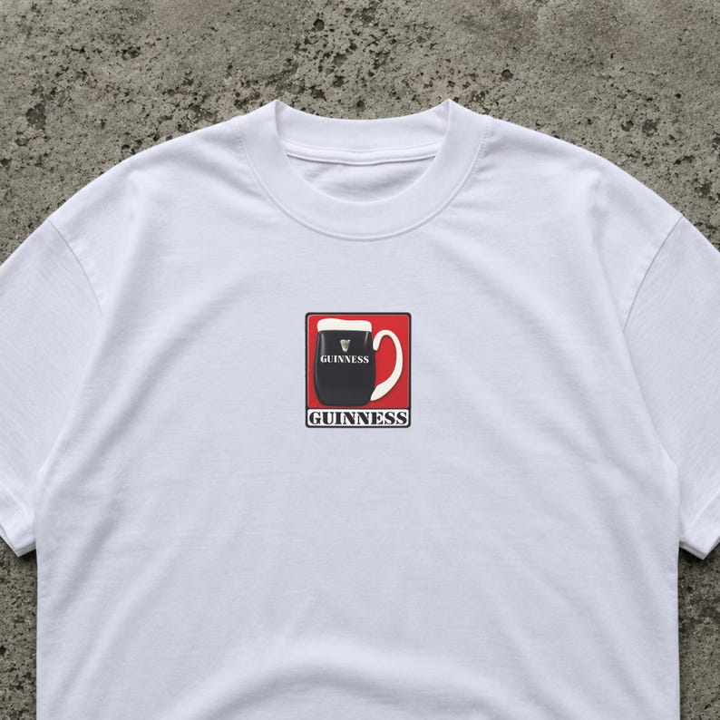 K&ouml;nnte beinhalten: Wei&szlig;es T-Shirt mit einem Guinness-Pint-Motiv. Das Design zeigt ein schwarzes Pint Stout in einem roten Quadrat, mit dem Guinness-Logo oberhalb und unterhalb der Pint-Illustration.