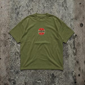 Pu&ograve; includere: T-shirt verde oliva con scollo tondo. La maglietta presenta un logo circolare con una stella rossa e la scritta "Heineken bier". La maglietta &egrave; realizzata in un materiale morbido.