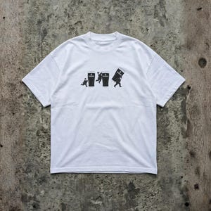 May include: White t-shirt featuring a black graphic of three figures interacting with Guinness pints. The design shows a person running towards a pint, another jumping over one, and a third carrying a tilted pint. The Guinness logo is visible.