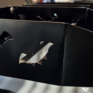 Puede incluir: Un organizador de metal negro con recortes en forma de murci&eacute;lago. El organizador tiene forma rectangular con m&uacute;ltiples compartimentos. Los recortes de murci&eacute;lago est&aacute;n espaciados uniformemente en la parte delantera, agregando un toque decorativo.