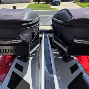 May include: Two black and gray storage bags mounted on a vehicle. The bags are labeled "NELSON-RIGG" and sit on black metal brackets with the "ROUSH" logo. The vehicle has red and white accents.