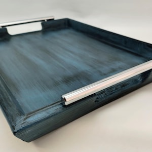 May include: Rectangular serving tray with a distressed blue finish and silver handles. The tray has a shallow depth and is designed for carrying items. The handles are mounted on the short sides of the tray.