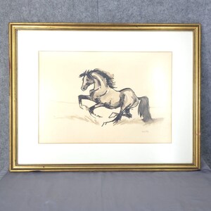 May include: A framed black and white ink drawing of a horse running. The horse is depicted in a dynamic pose with its head turned to the side. The drawing is on a cream-colored paper and is framed in a gold frame.
