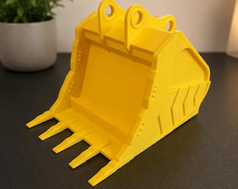 May include: A bright yellow excavator bucket model featuring a reinforced cutting edge with four distinct teeth, side wall ribbing, and two top mounting lugs. The construction equipment replica is rendered in a solid, matte yellow finish.