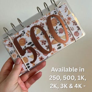 May include: A clear, ring-bound organiser with a floral autumn-themed insert. The number "500" is cut from copper-coloured material and is attached to the front. The text "Available in 250, 500, 1K, 2K, 3K & 4K - see images" is printed on the right side.