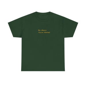 K&ouml;nnte beinhalten: Ein dunkelgr&uuml;nes T-Shirt mit dem goldenen Text "Be Where You're Wanted". Das T-Shirt hat einen Rundhalsausschnitt und ist aus einem weichen Stoff gefertigt. Der Text ist mittig auf der Brust platziert.